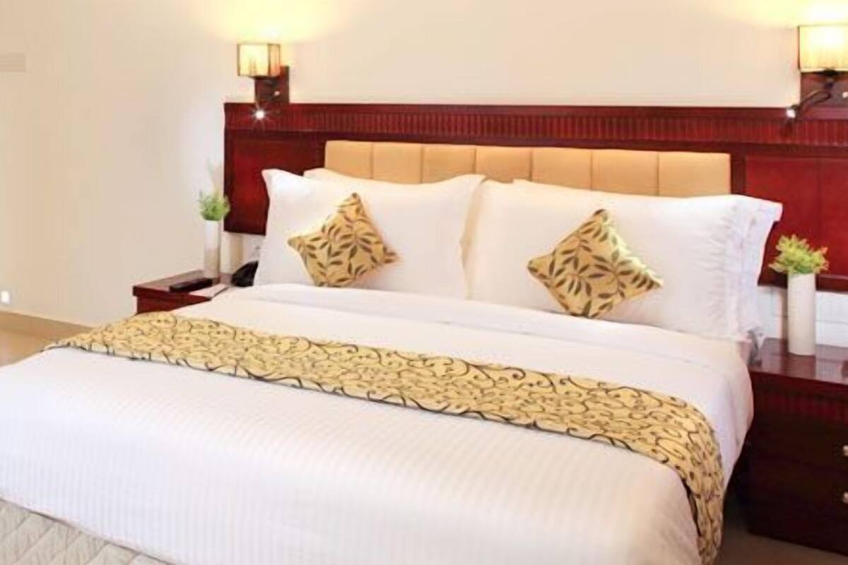 A hotel room with a bed, a chair, a small table with fruit, and a television on the wall.