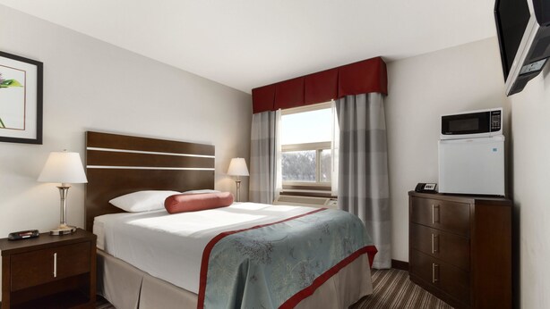 A hotel room with a bed, nightstands, a desk, a microwave, and a window with curtains. - Super 8 by Wyndham Saskatoon Near Downtown (Saskatoon)