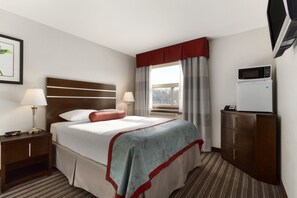 Quarto de hotel com cama, mesas de cabeceira, escrivaninha, micro-ondas e janela com cortinas.