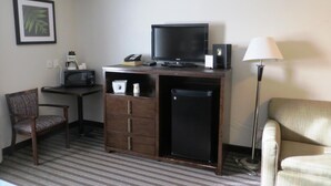 A hotel room with a desk, a television, a refrigerator, a chair, and a lamp. - Super 8 by Wyndham Saskatoon Near Downtown (Saskatoon)