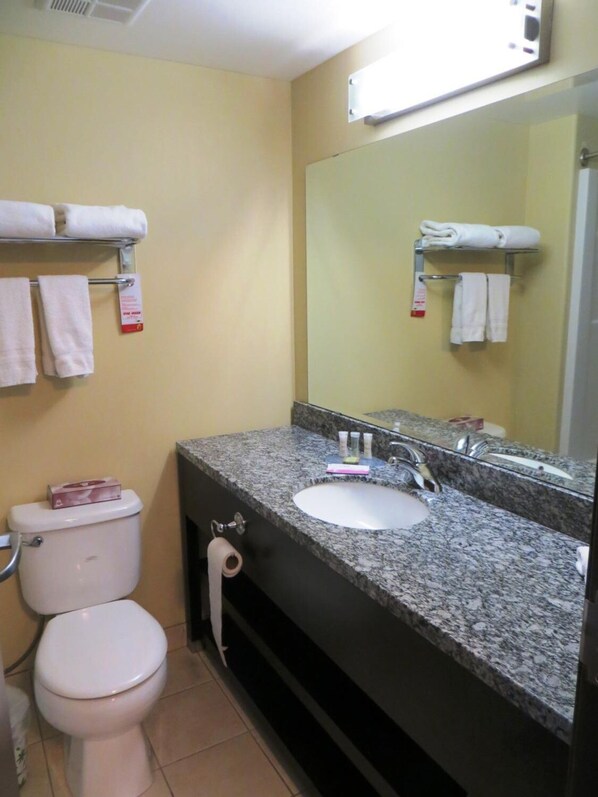 A bathroom with a toilet, sink, and mirror. There are towels on a rack and a box on the toilet.