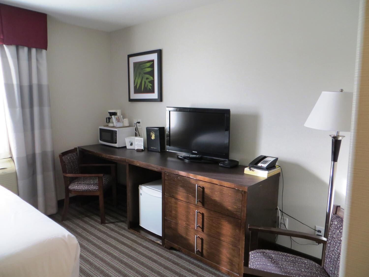A hotel room with a wooden desk, a television, a microwave, a coffee maker, a telephone, and a bed.