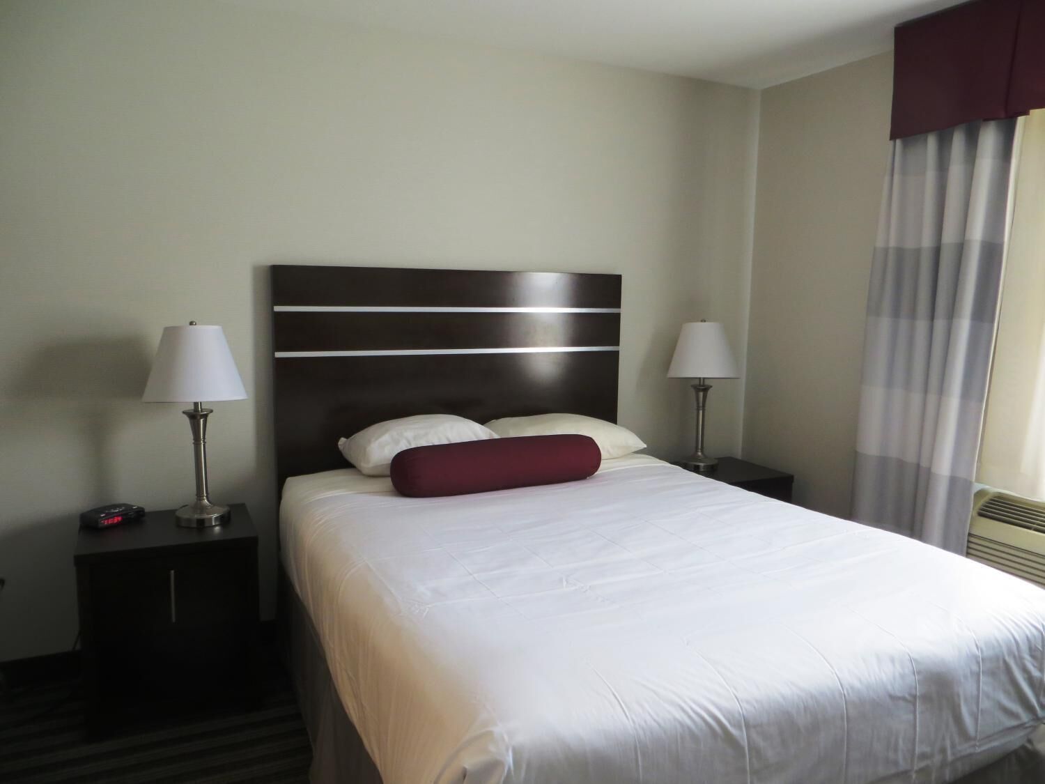 Ein Hotelzimmer mit einem großen Bett, zwei Nachttischen, zwei Lampen und einem fensterbepflanzten Fenster.
