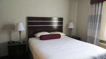 Ein Hotelzimmer mit einem großen Bett, zwei Nachttischen, zwei Lampen und einem fensterbepflanzten Fenster.