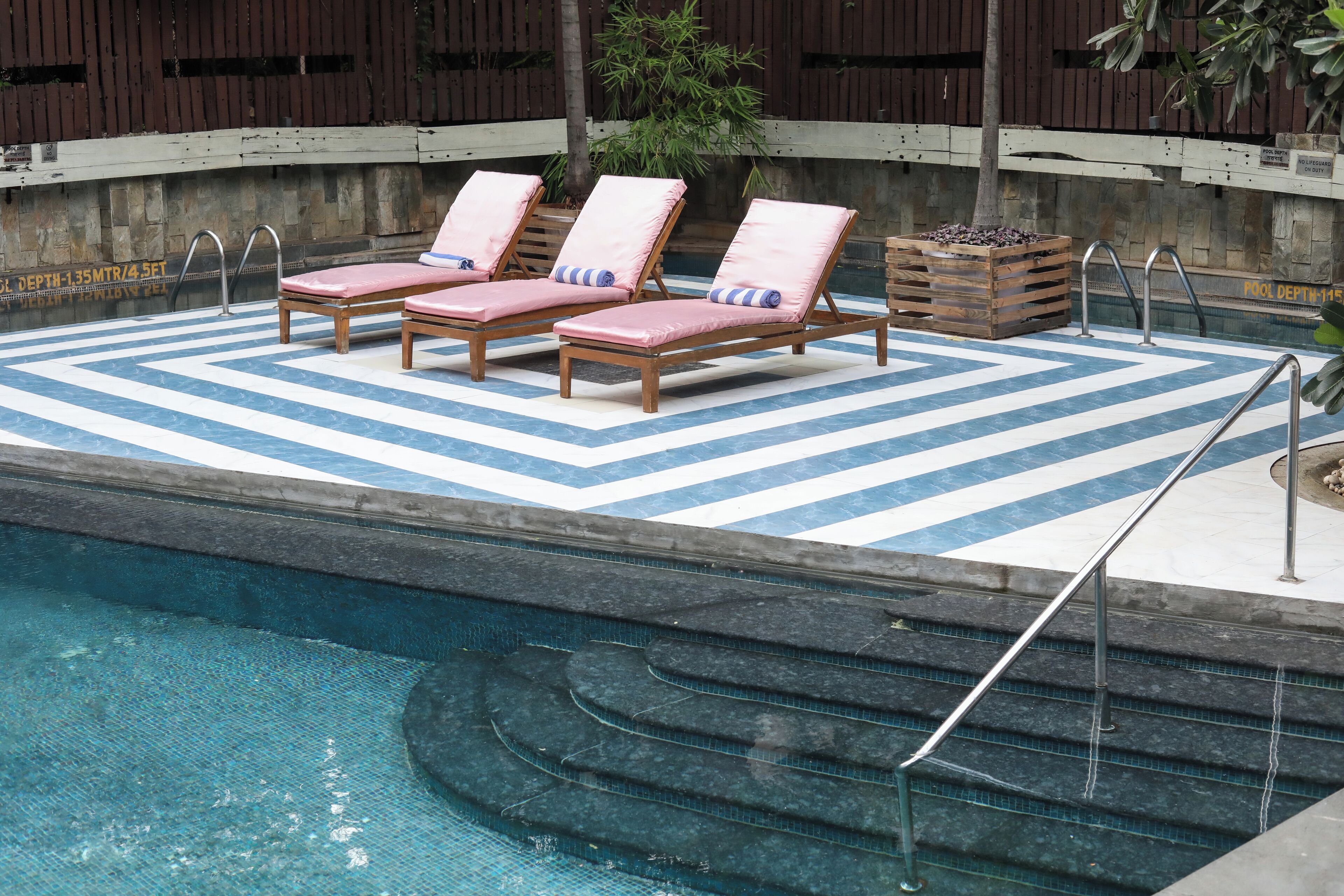 Uma área de piscina com três espreguiçadeiras, um deck de madeira e um muro de pedra.