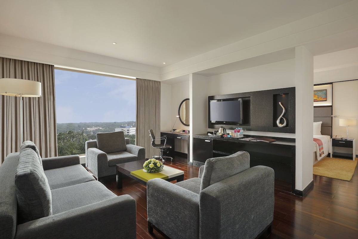 A modern hotel room with a living area, kitchenette, and a large window offering a city view.