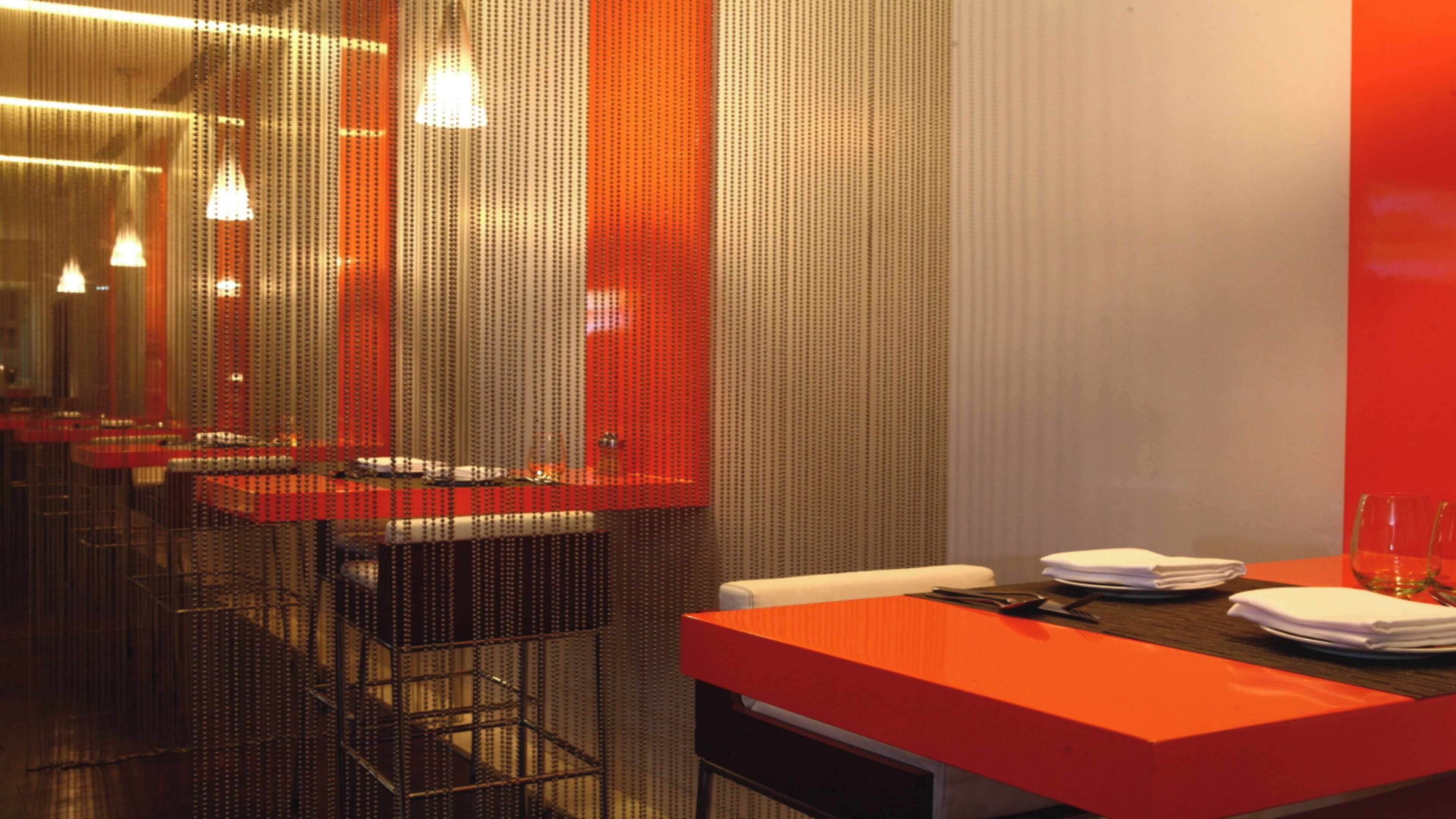 Un interior de restaurante moderno con una barra alargada, sillas de metal y una pared de acento roja.