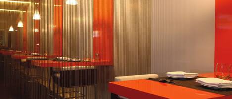 Un interno ristorante moderno con un lungo bancone, sedie in metallo e una parete di colore rosso.