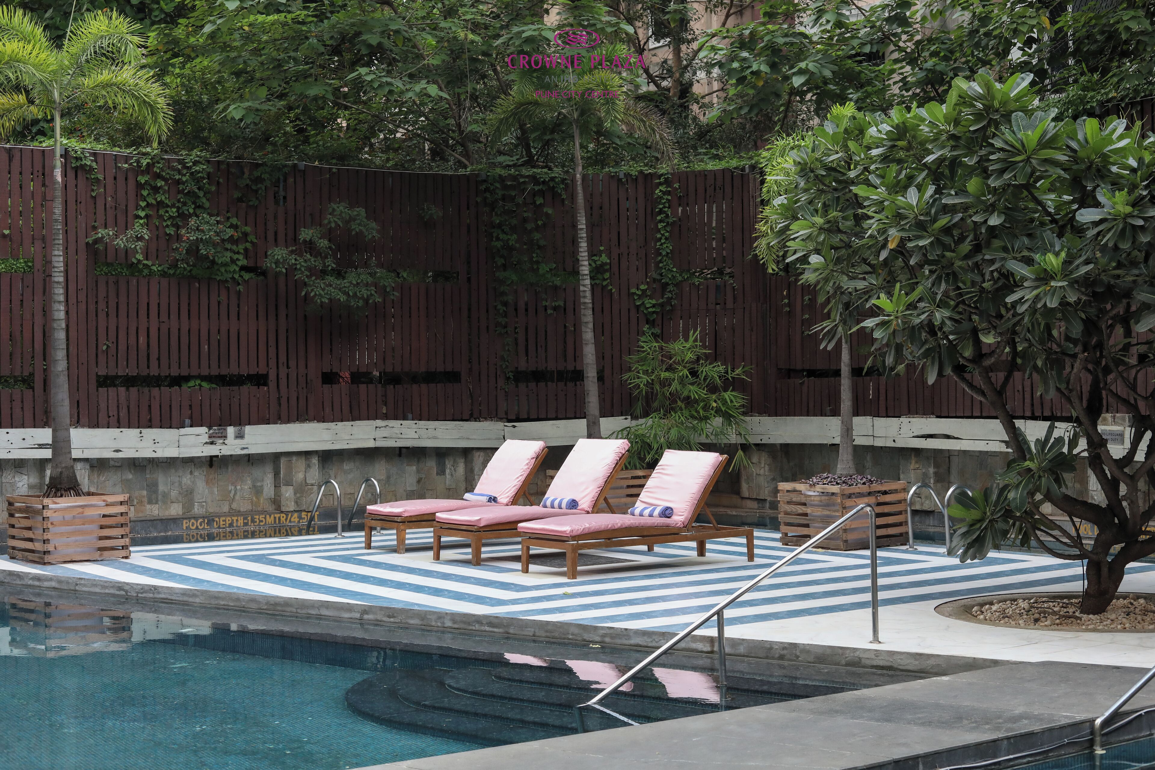 A pool area with three lounge chairs, a wooden fence, and a tree.