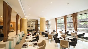 A spacious dining area with multiple tables and chairs, large windows, and a high ceiling.
