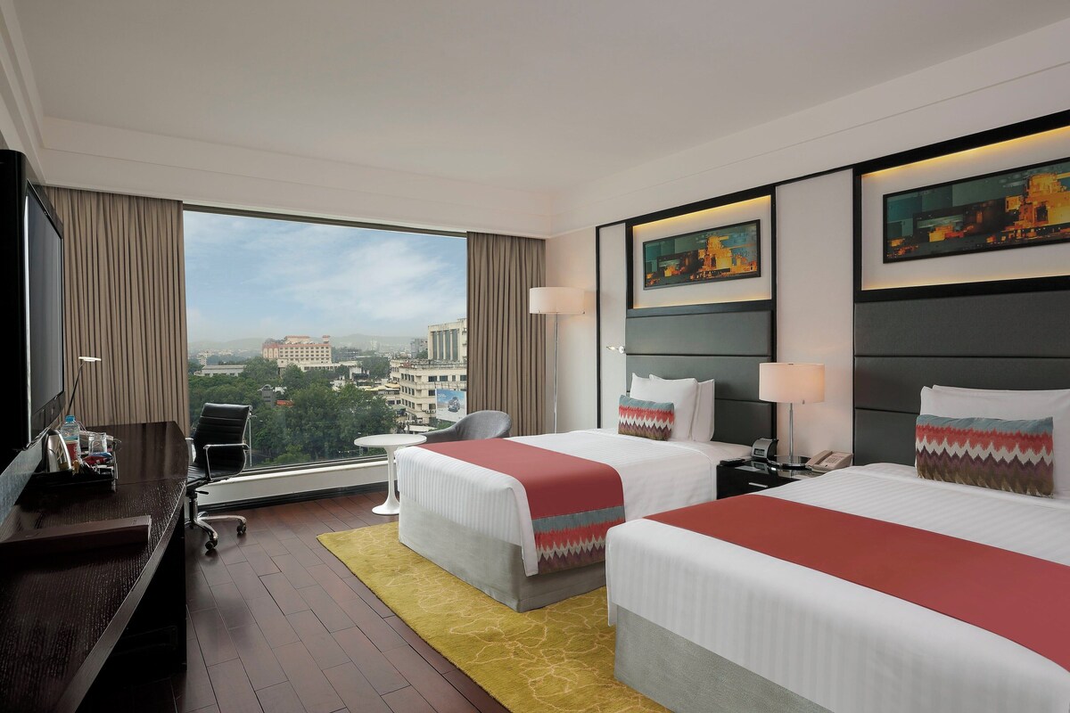 Une chambre d’hôtel avec deux lits, un bureau, une chaise et une vue sur la ville.