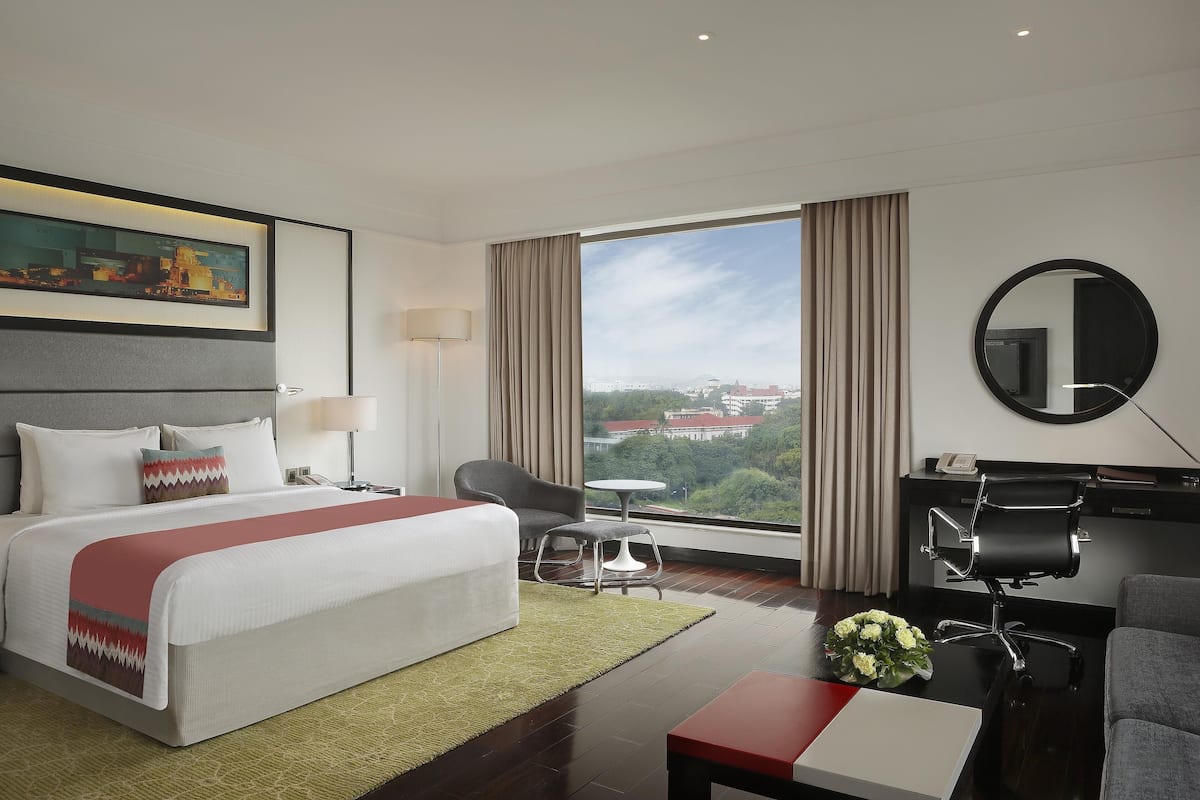 A modern hotel room with a large bed, a desk, a chair, and a view of the city.