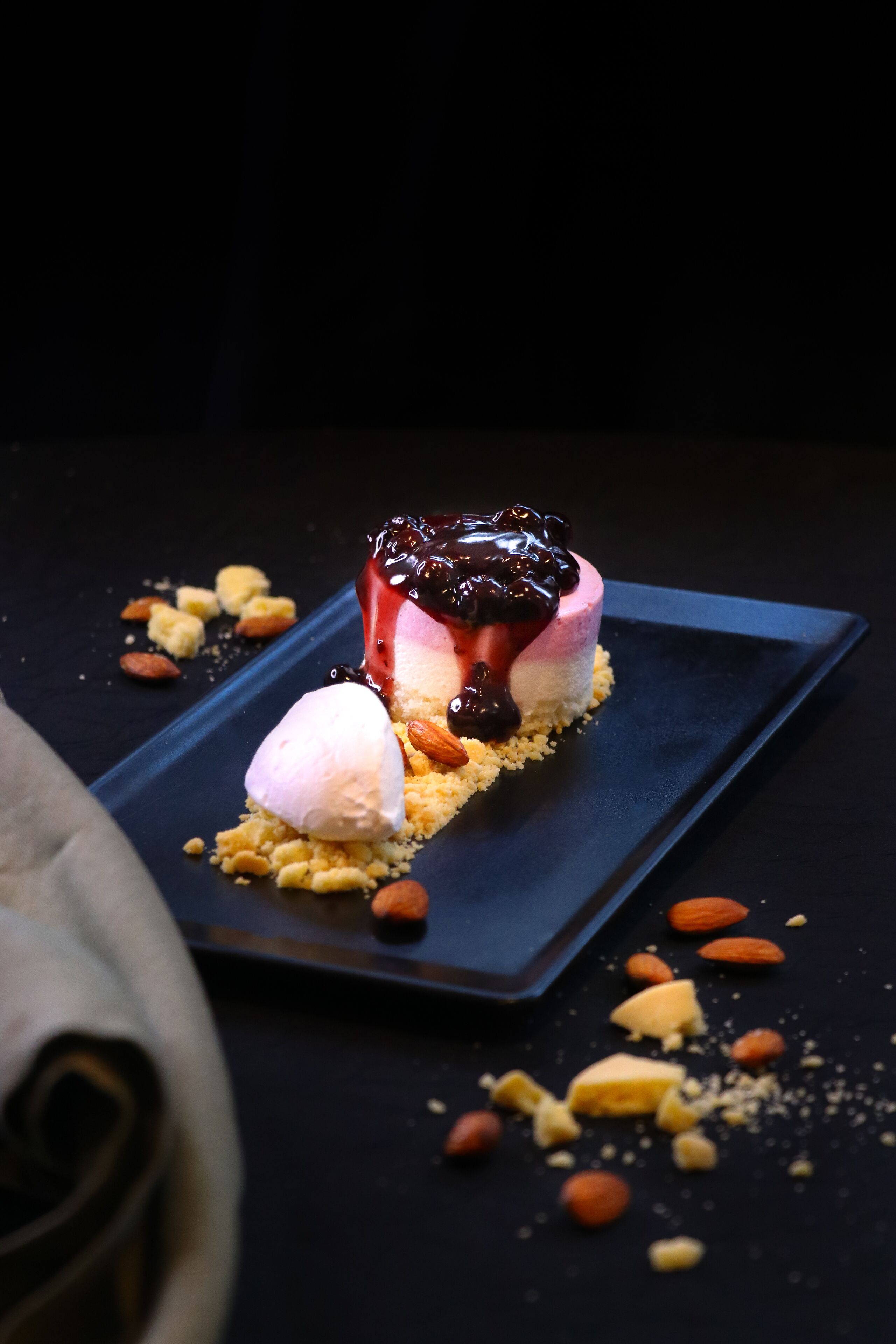 A dessert on a dark plate with almonds and crumbs.