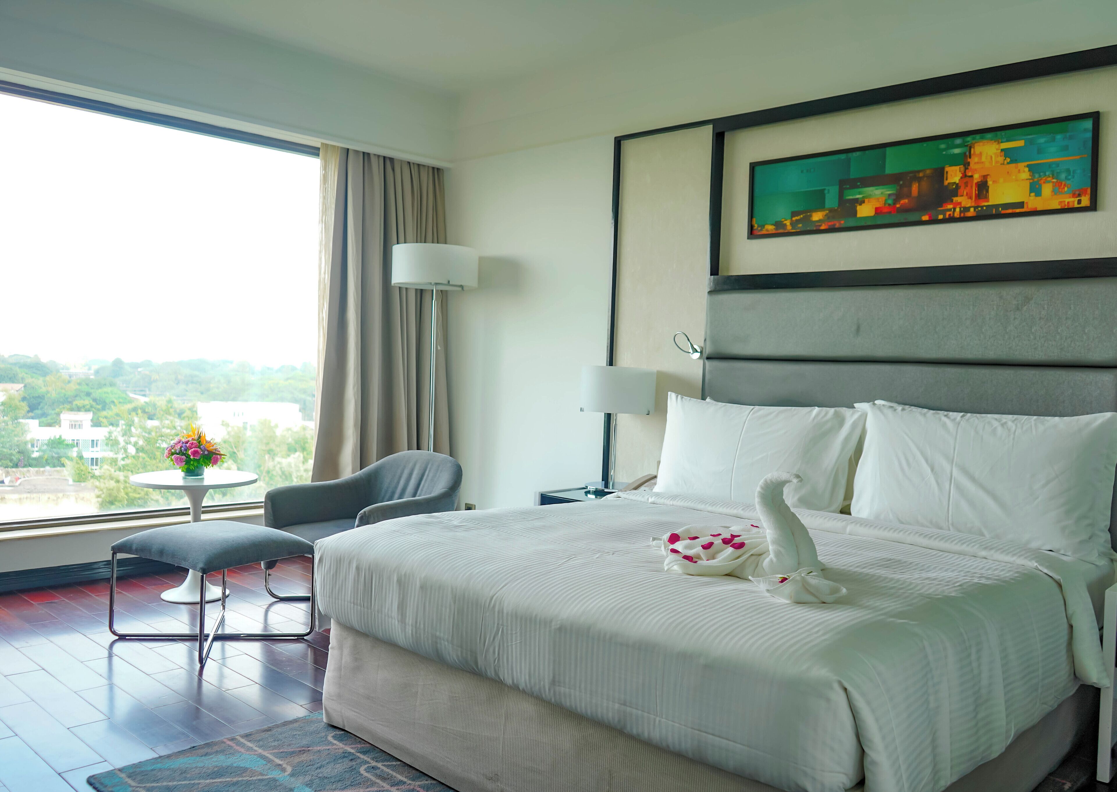 Habitación de hotel con una cama grande, una silla, una mesita y un cuadro en la pared.