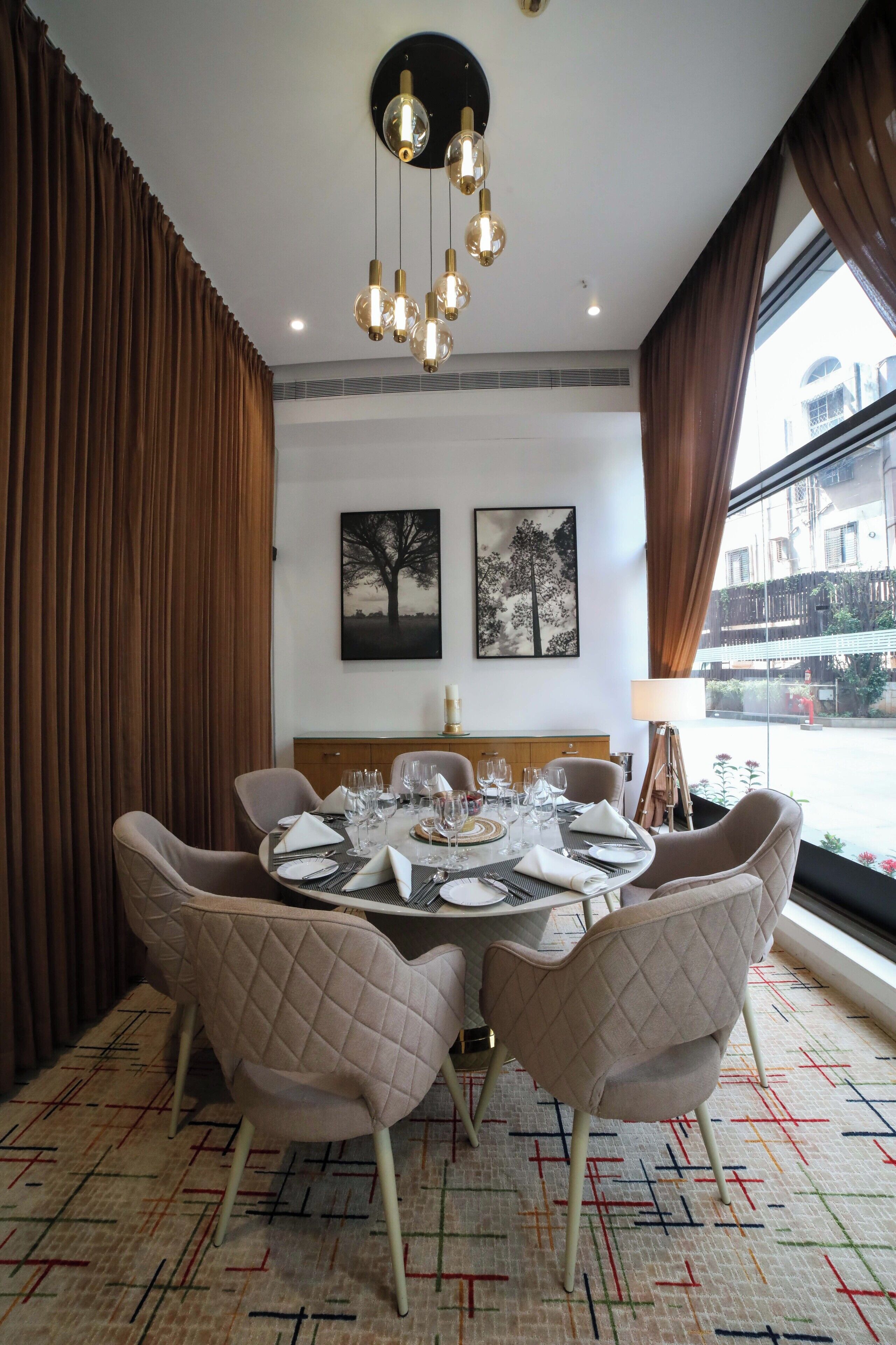 Uma sala de jantar com uma mesa redonda posta para quatro pessoas, cadeiras acolchoadas, um lustre e obras de arte nas paredes.