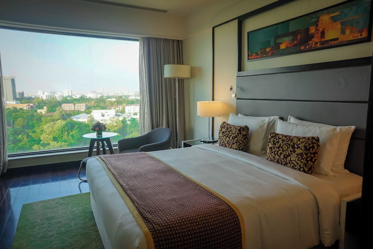 A hotel room with a large bed, a desk, a chair, and a view of the city.