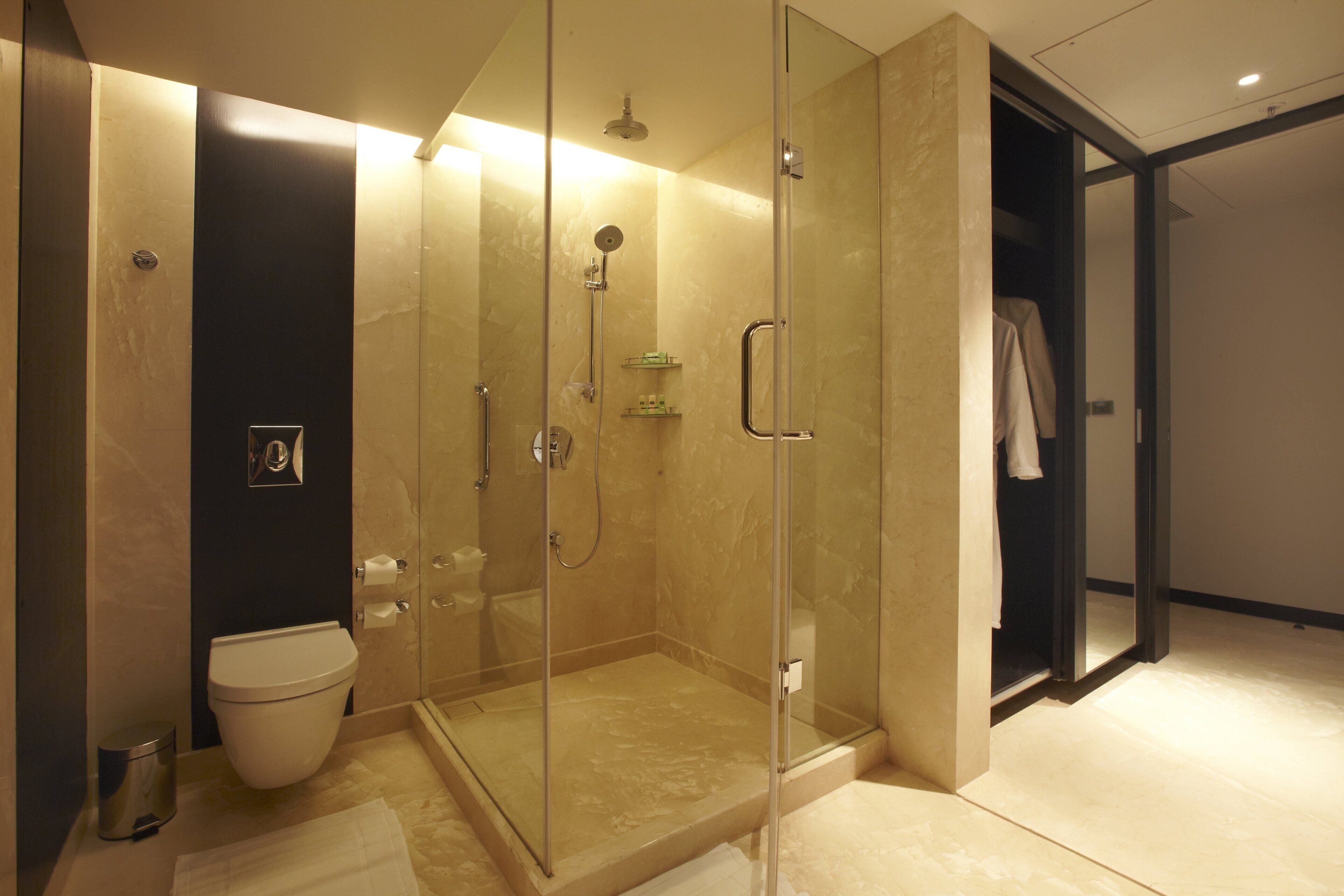 A modern bathroom with a glass-enclosed shower, a toilet, and a walk-in closet.