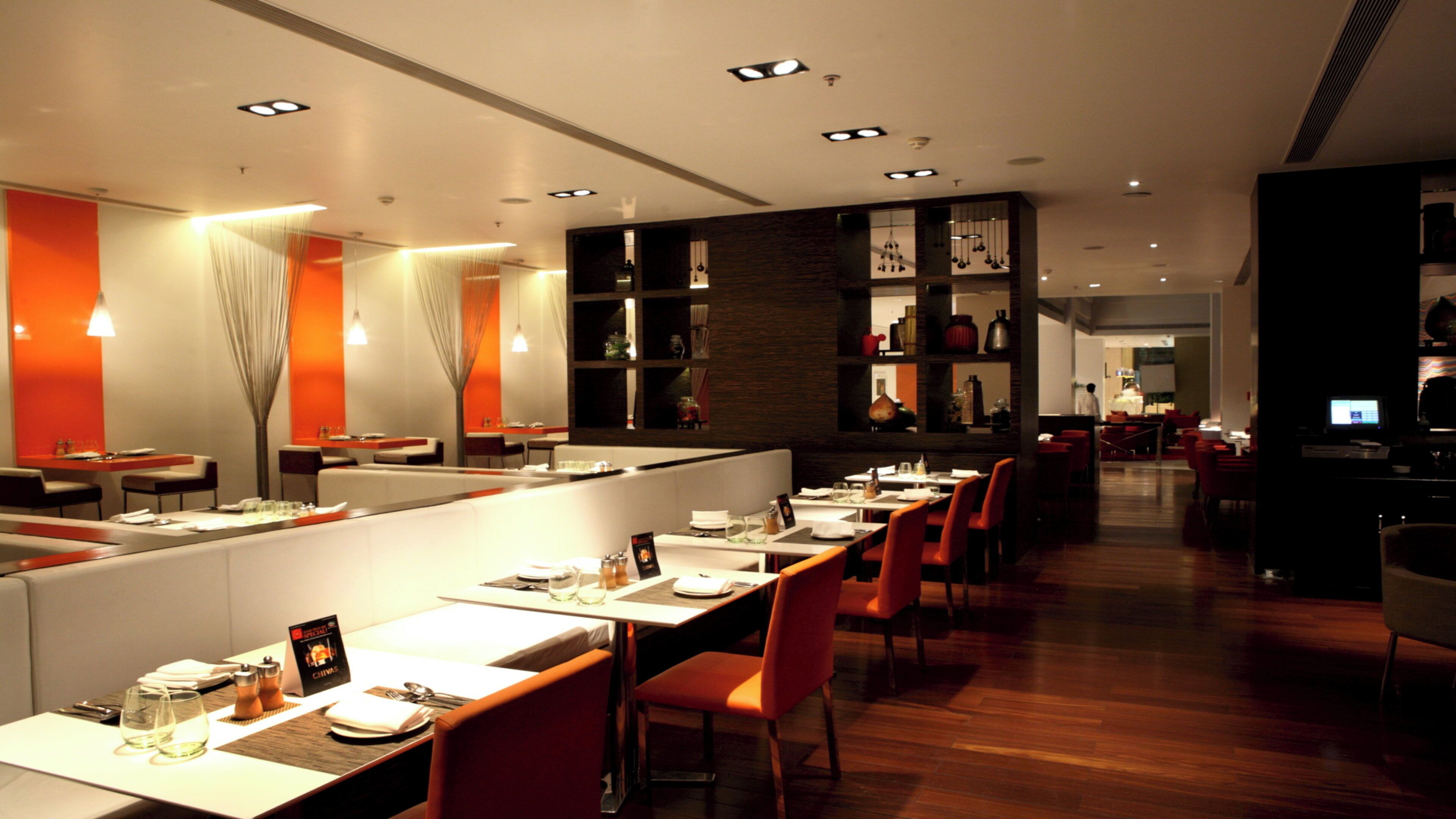 A modern restaurant with long communal tables, individual booths, and a bar area.