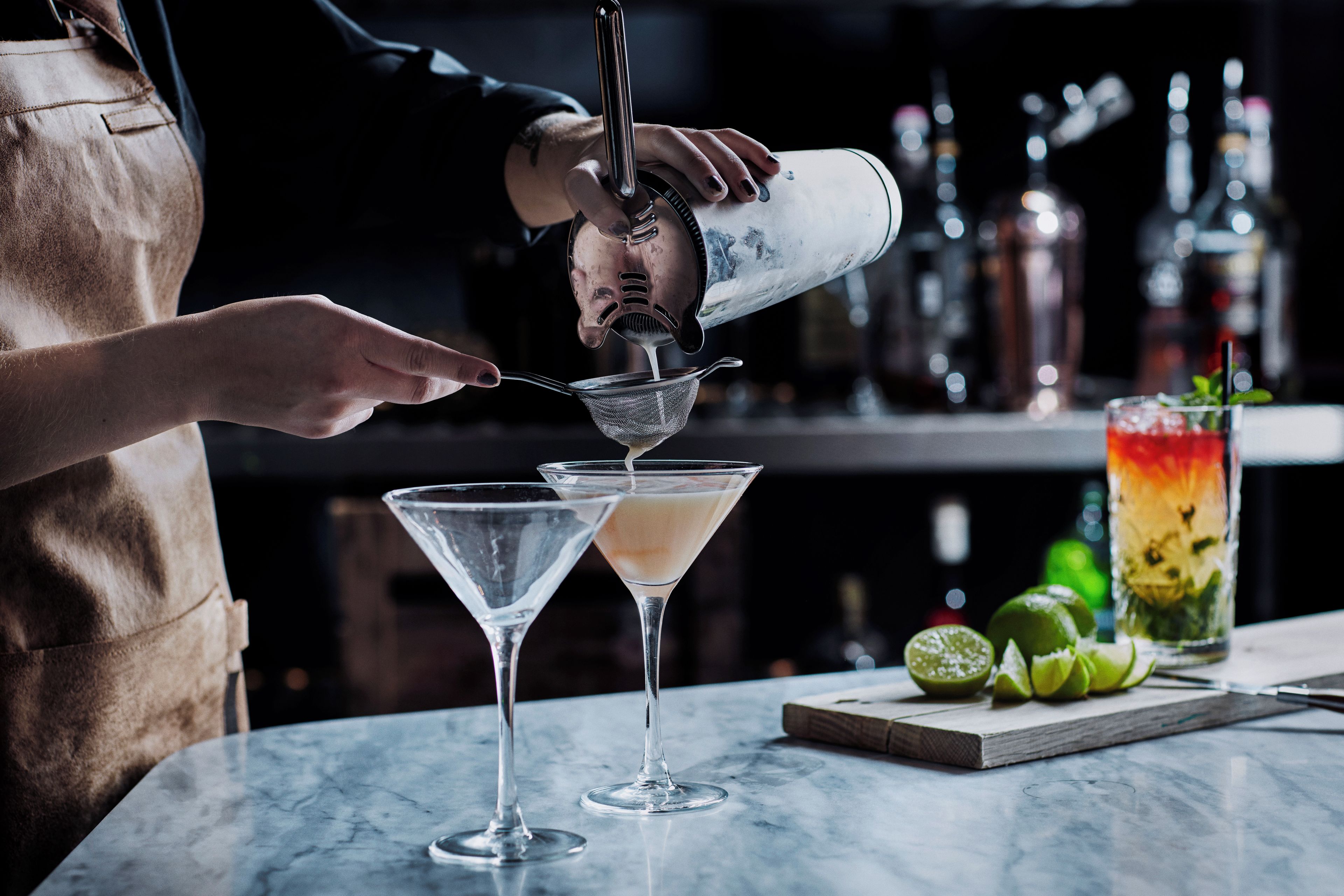 A bartender pouring a drink into a martini glass.