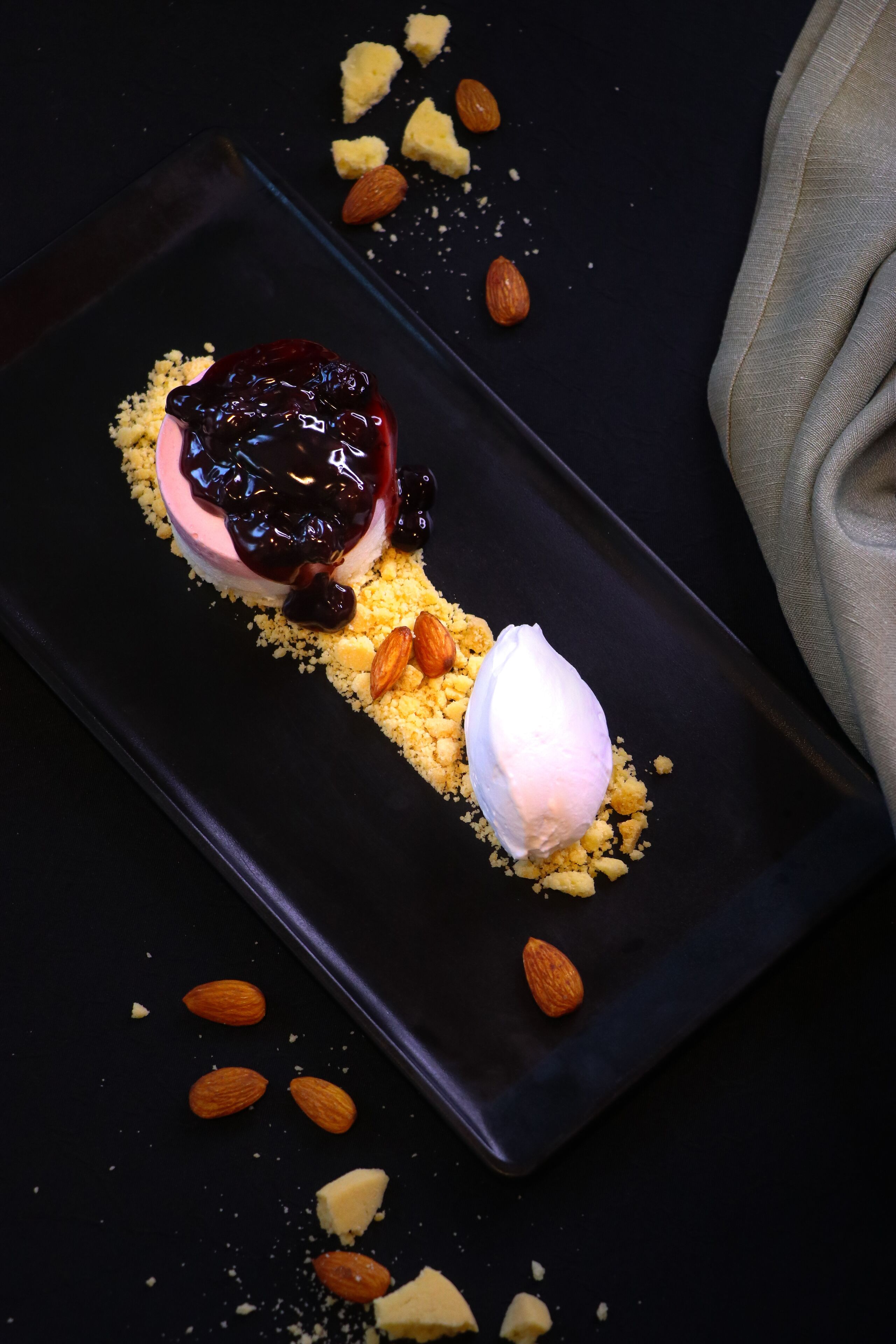 A dessert on a black plate with a crumbled base, almonds, and a scoop of ice cream.