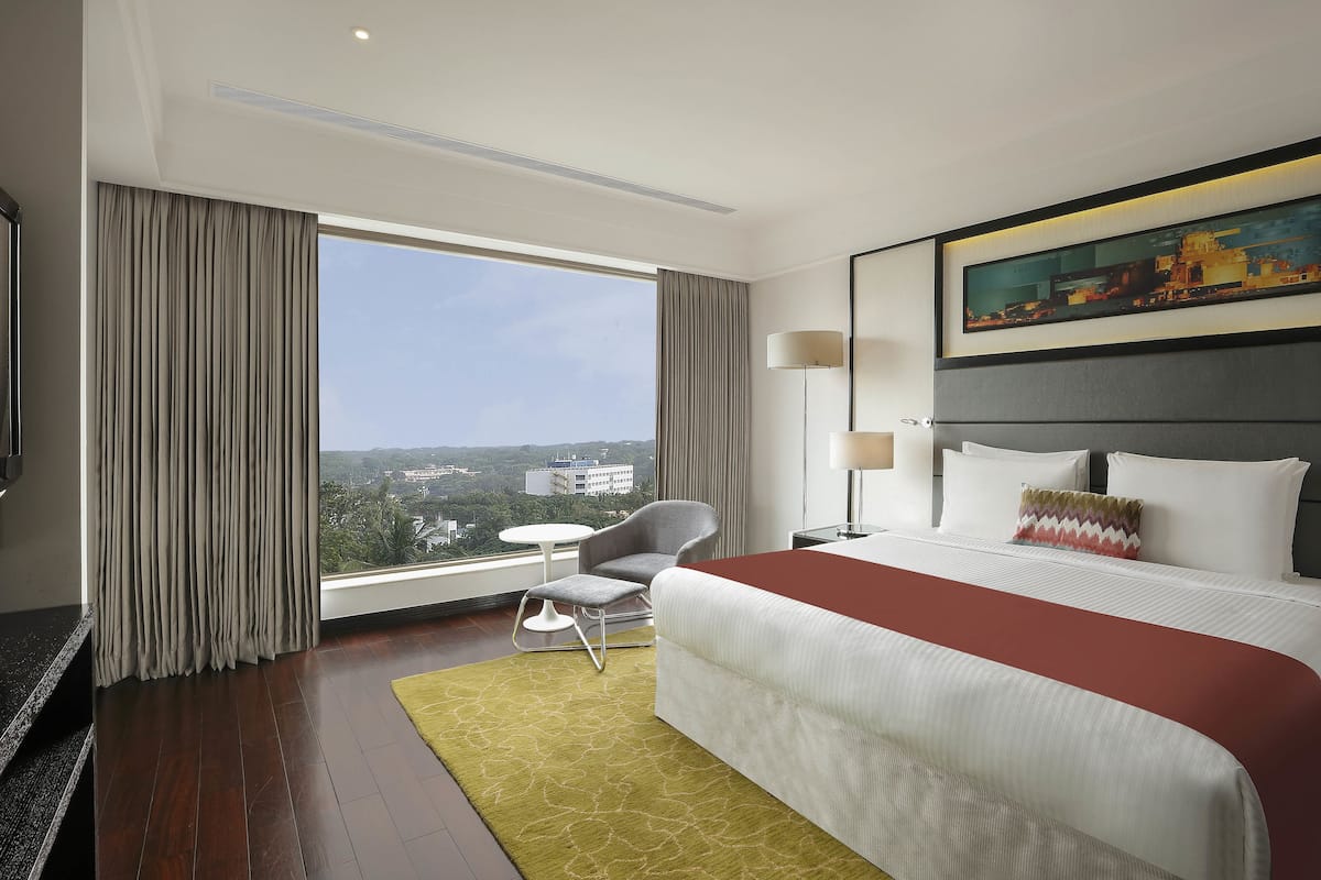 A hotel room with a large bed, a chair, a small table, and a painting on the wall.