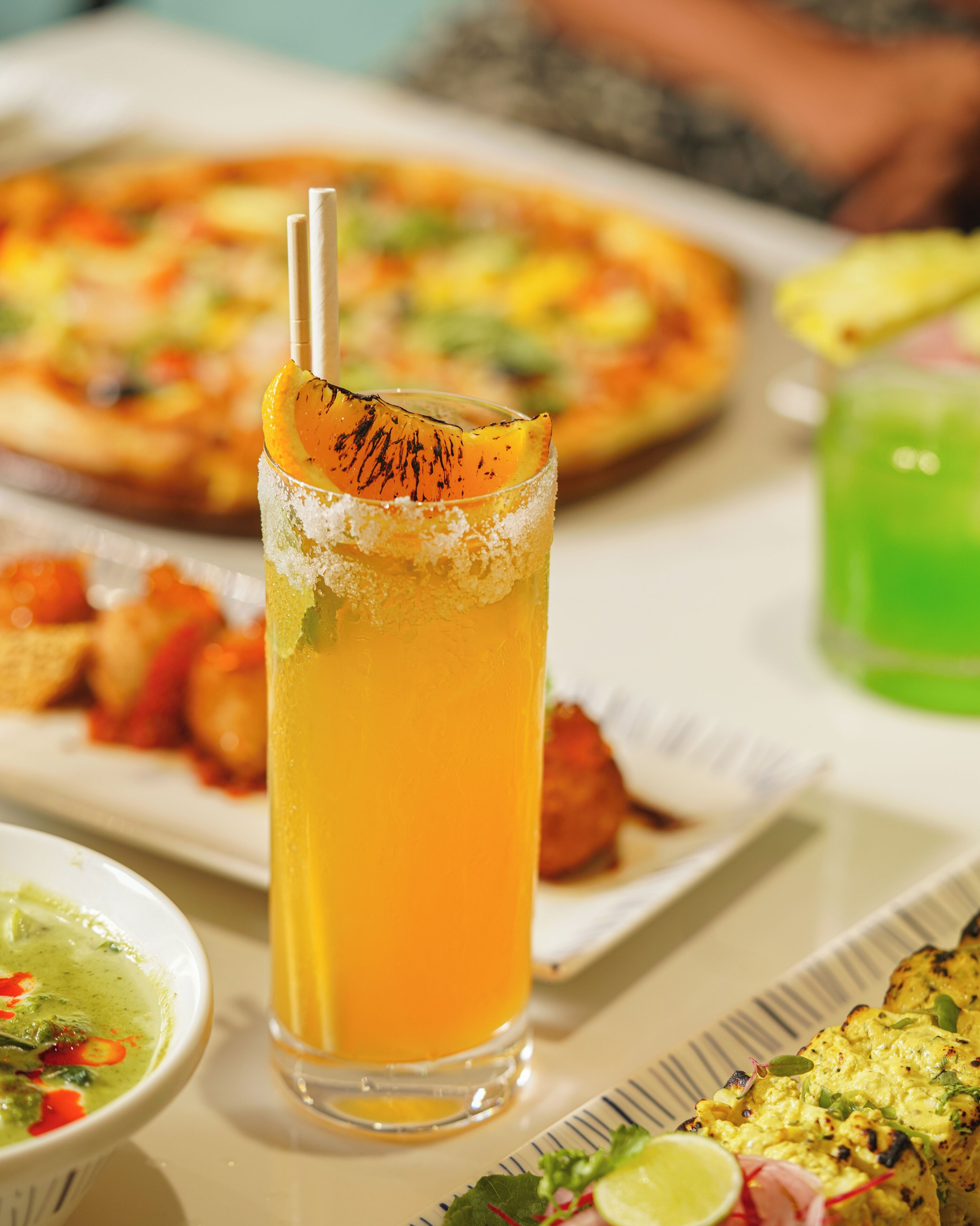 A table with a glass of orange juice, a pizza, and various dishes.