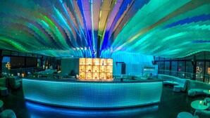 A modern bar area with a central illuminated counter, seating arrangements, and a ceiling with a unique light pattern.