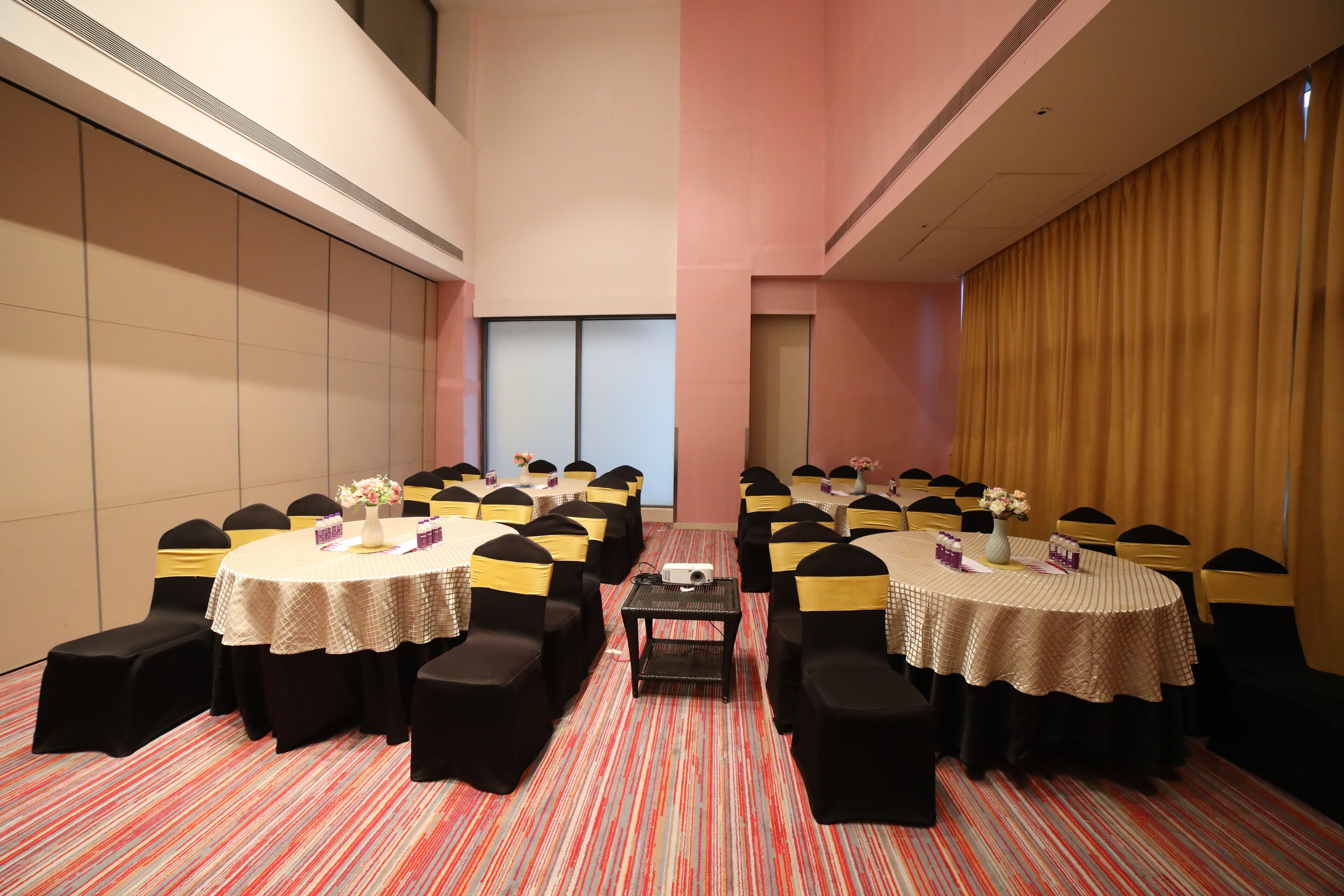 A conference room with multiple tables, black chairs with yellow sashes, and a red-striped carpet.