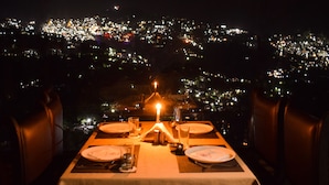 Mesa para dos con vela, platos y copas, con vista a un paisaje urbano nocturno.