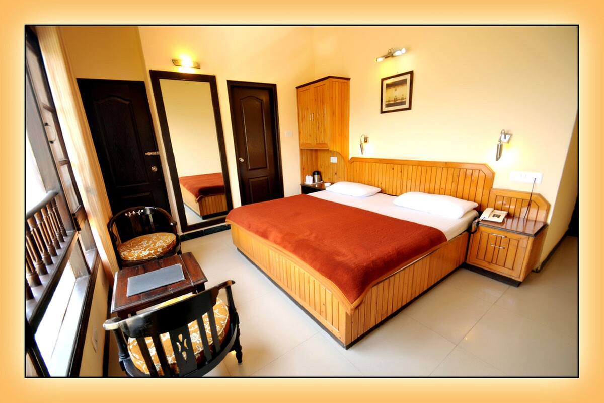 A hotel room with a large bed, a wooden wardrobe, a bedside table with a lamp, and a chair.