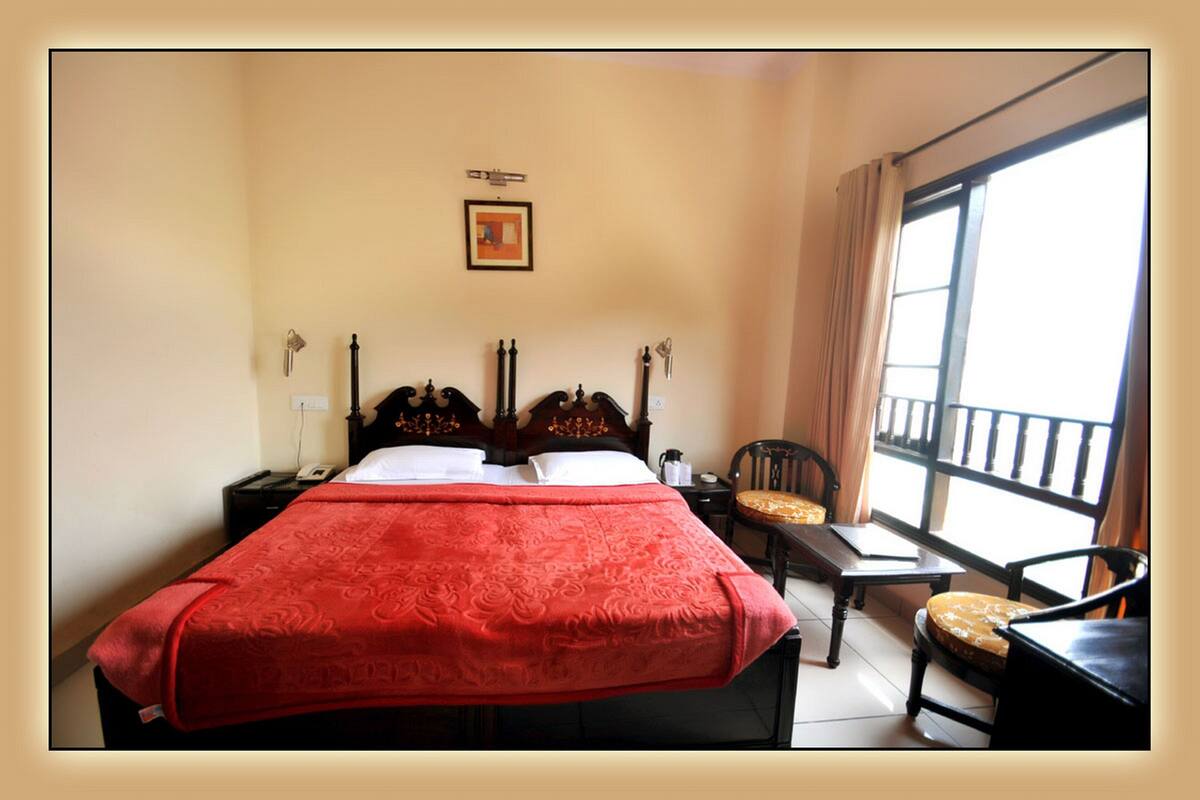 A hotel room with a bed, a chair, a table, and a window with curtains.
