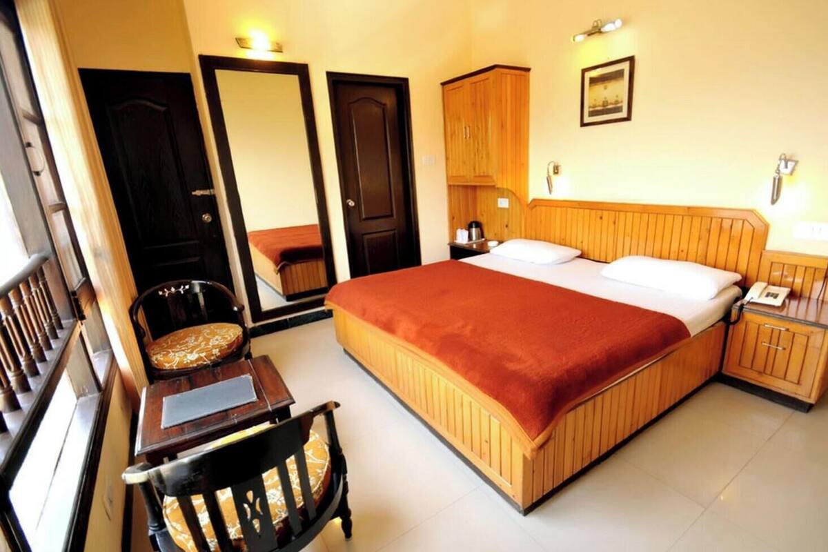 A hotel room with a large bed, a desk, a chair, a wardrobe, and a mirror.
