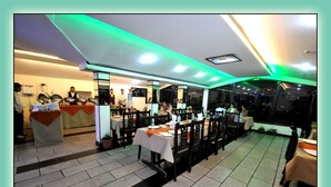 Un restaurante con varias mesas, una zona de recepción y vistas a la ciudad de noche.