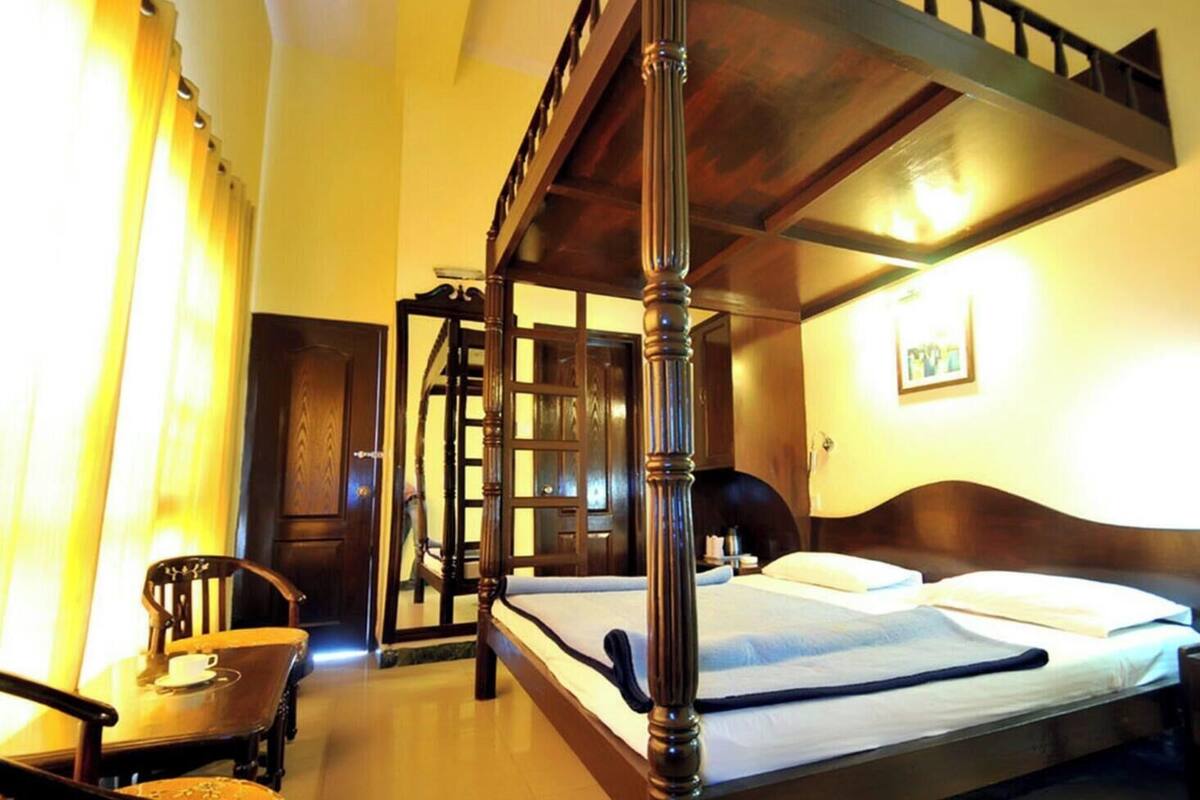 A four-poster bed with a wooden headboard, a chair, and a bedside table in a hotel room.