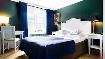 Una camera d'albergo con un letto, una scrivania, una sedia, un comodino e una finestra con tende.