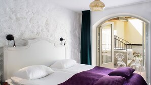 Un dormitorio con cabecera blanca, colcha morada y vista a un área de estar exterior a través de un arco.