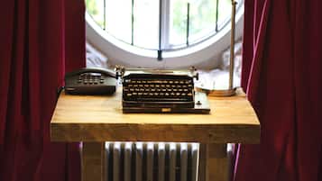 Escritorio de madera con máquina de escribir y teléfono, frente a una ventana con vistas a zonas verdes.