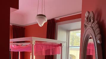 A four-poster bed with white bedding, a large mirror, and a window with curtains.