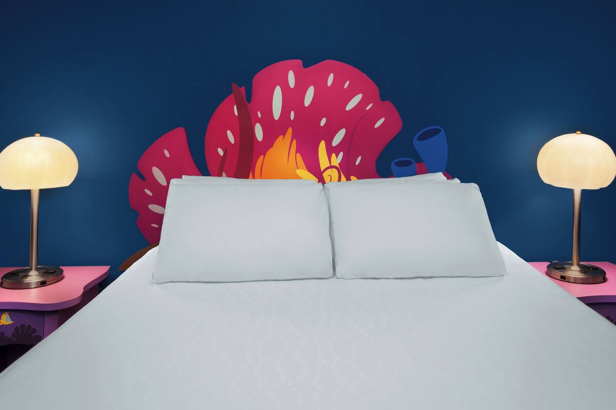 A bed with two bedside lamps, a large decorative headboard with a flame design, and a blue wall.