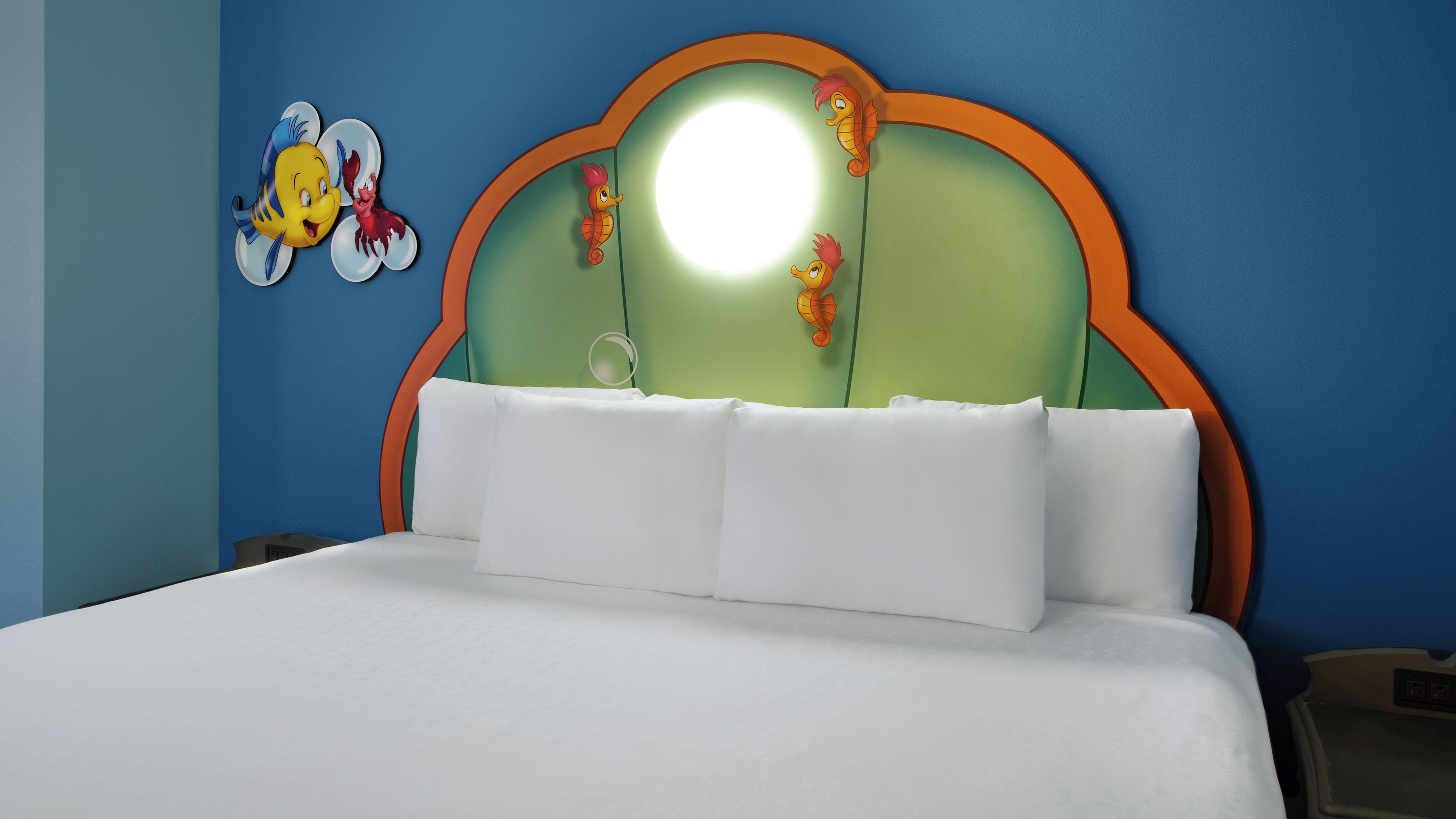 A bed with white bedding, a green headboard with orange trim, and a wall with a cartoon character.