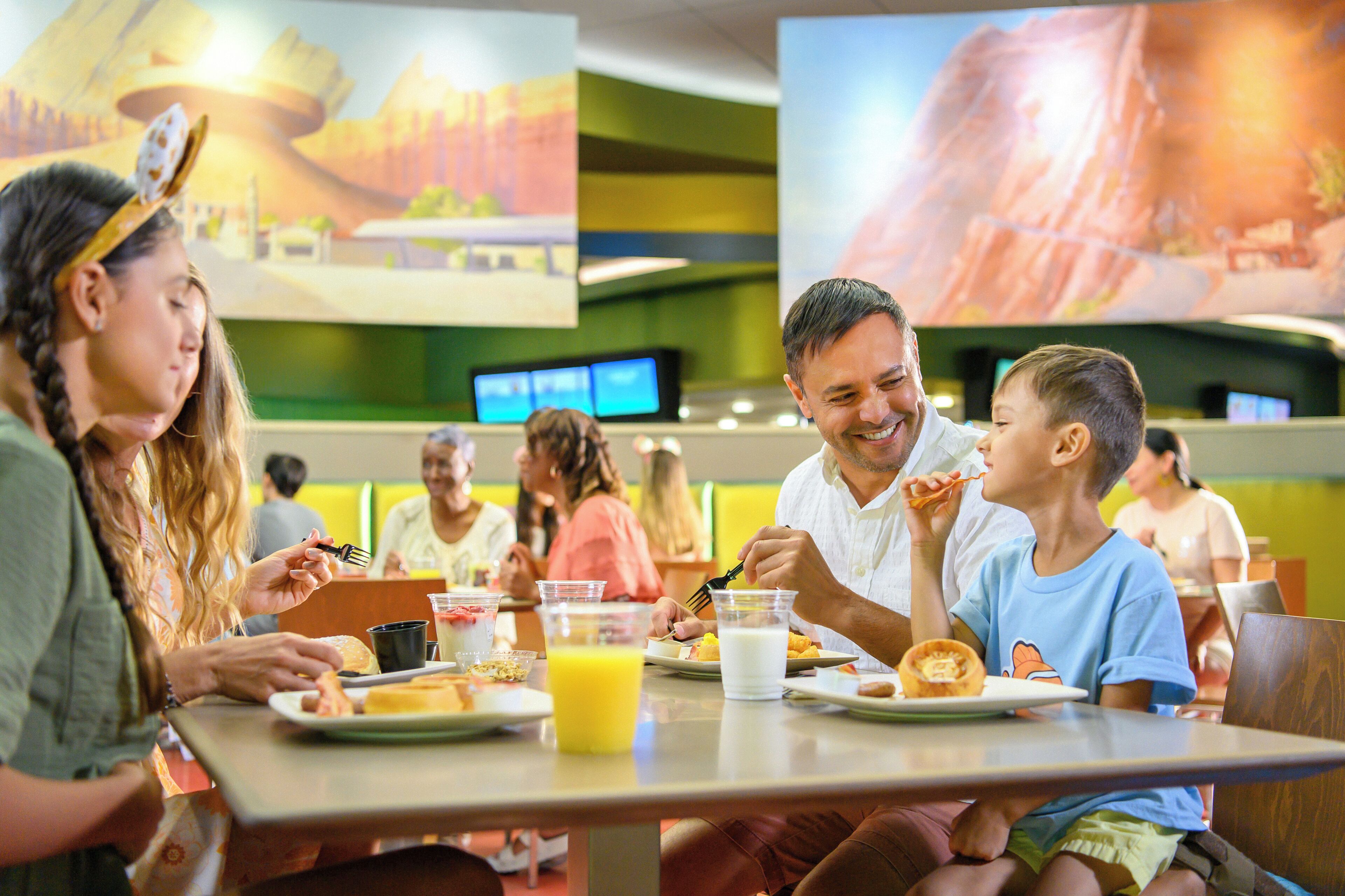 Une famille est assise à une table dans un restaurant, et un grand écran diffuse des images d’un paysage.