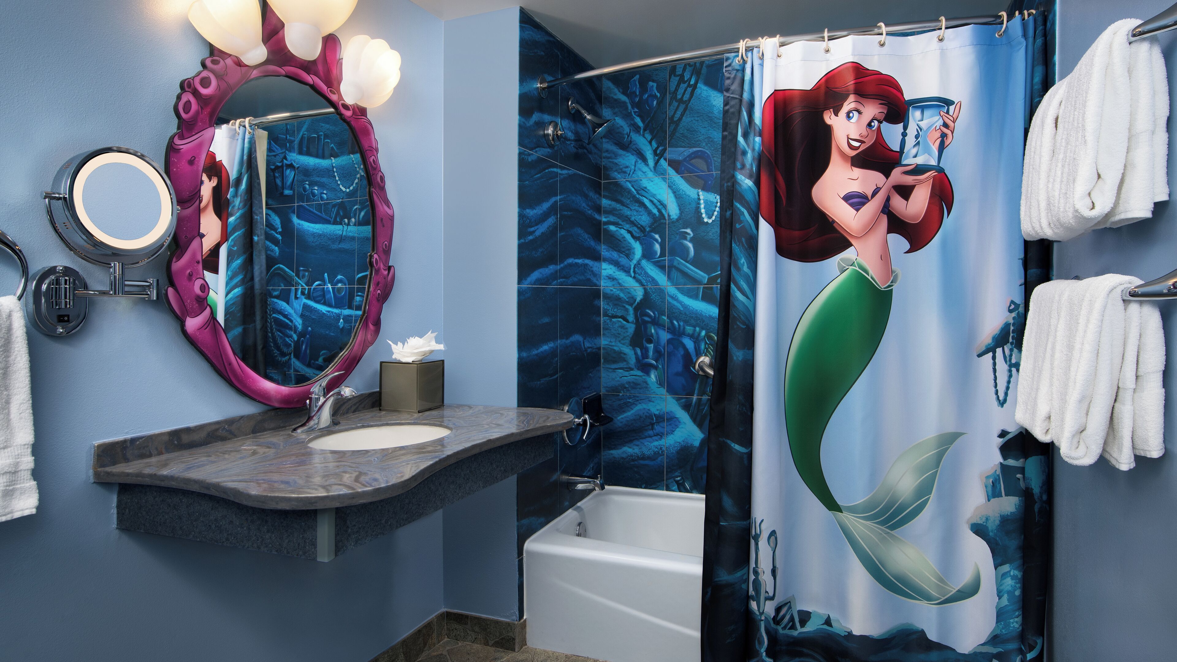 A bathroom with a large mirror, a sink, a bathtub, and a shower curtain with a mermaid design.