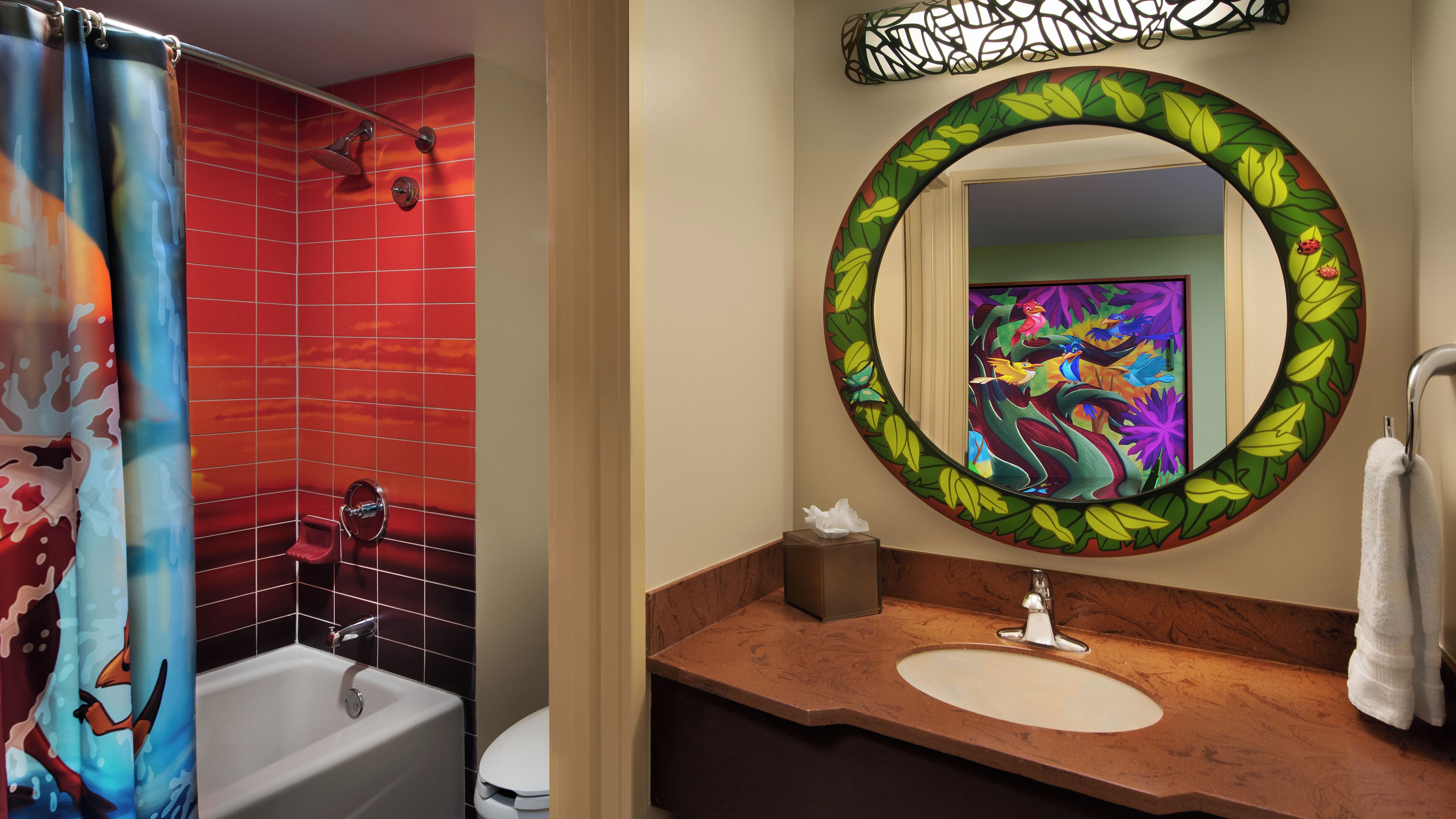A bathroom with a red tiled shower, a white bathtub, a round mirror with a leaf design, and a wooden vanity with a sink.