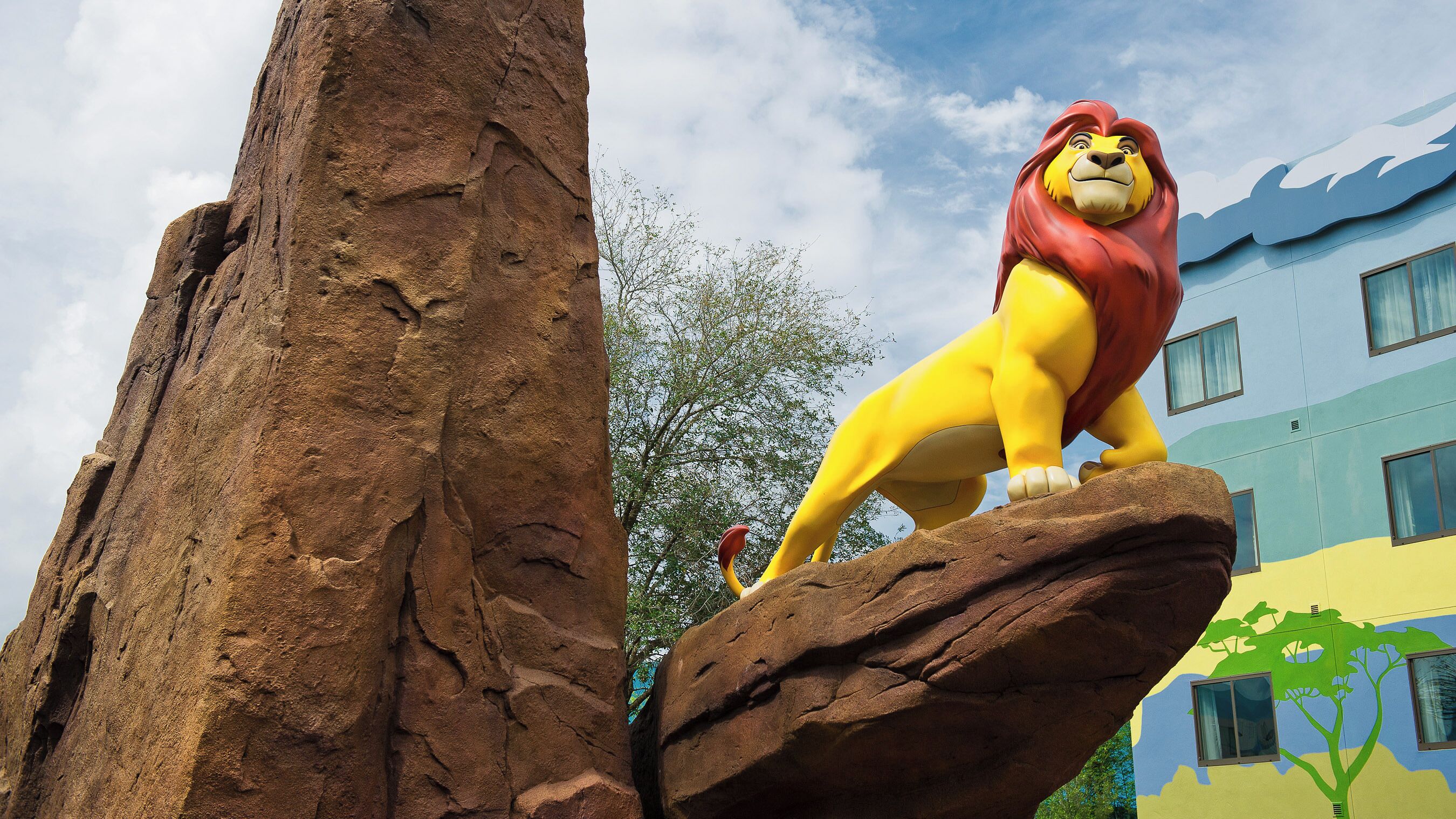 Une grande statue de lion, posée sur un rocher, avec un bâtiment en arrière-plan.
