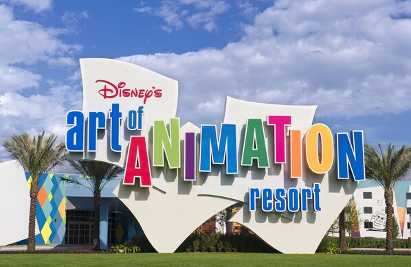 Das Äußere des Disney's Art of Animation Resort mit einem großen Schild mit farbenfrohen Schriftzügen und Palmen im Vordergrund.
