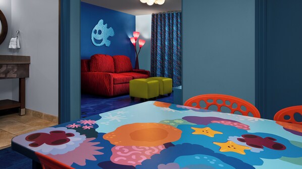 A room with a colorful table, a red sofa, and a blue wall with a shark decoration.