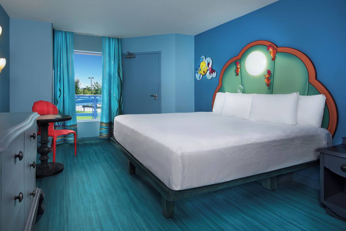 A hotel room with a large bed, a desk, a chair, and a view of the outside.