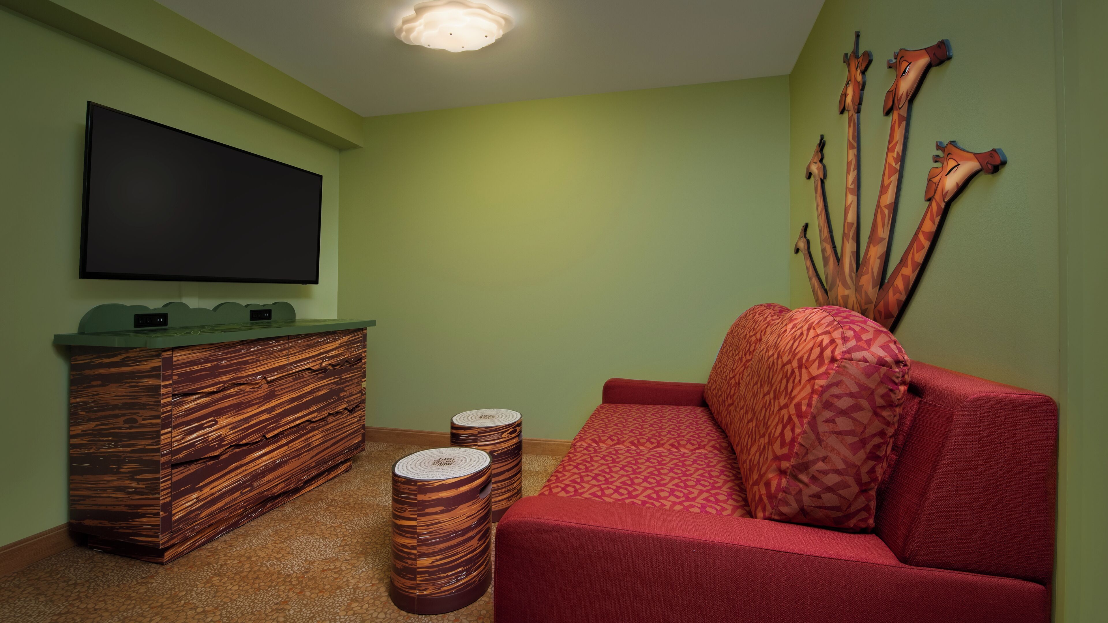 Une pièce avec un mur vert, un téléviseur à écran plat fixé au-dessus d’un meuble en bois, un canapé rouge et un élément décoratif mural.