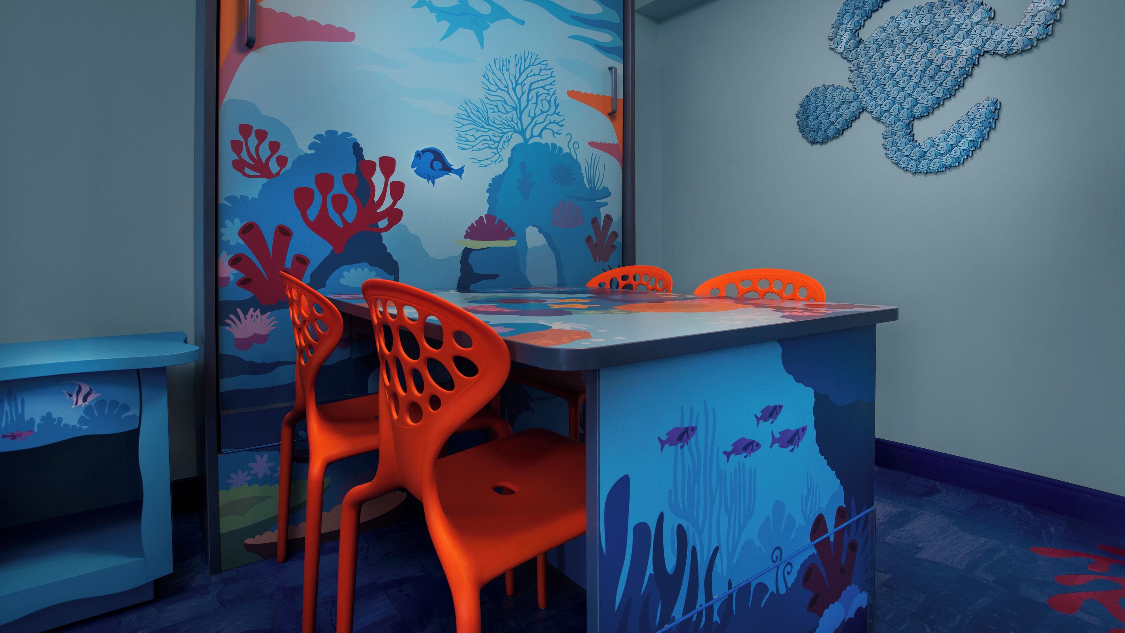 A children's playroom with a table and chairs, decorated with ocean-themed wall art.