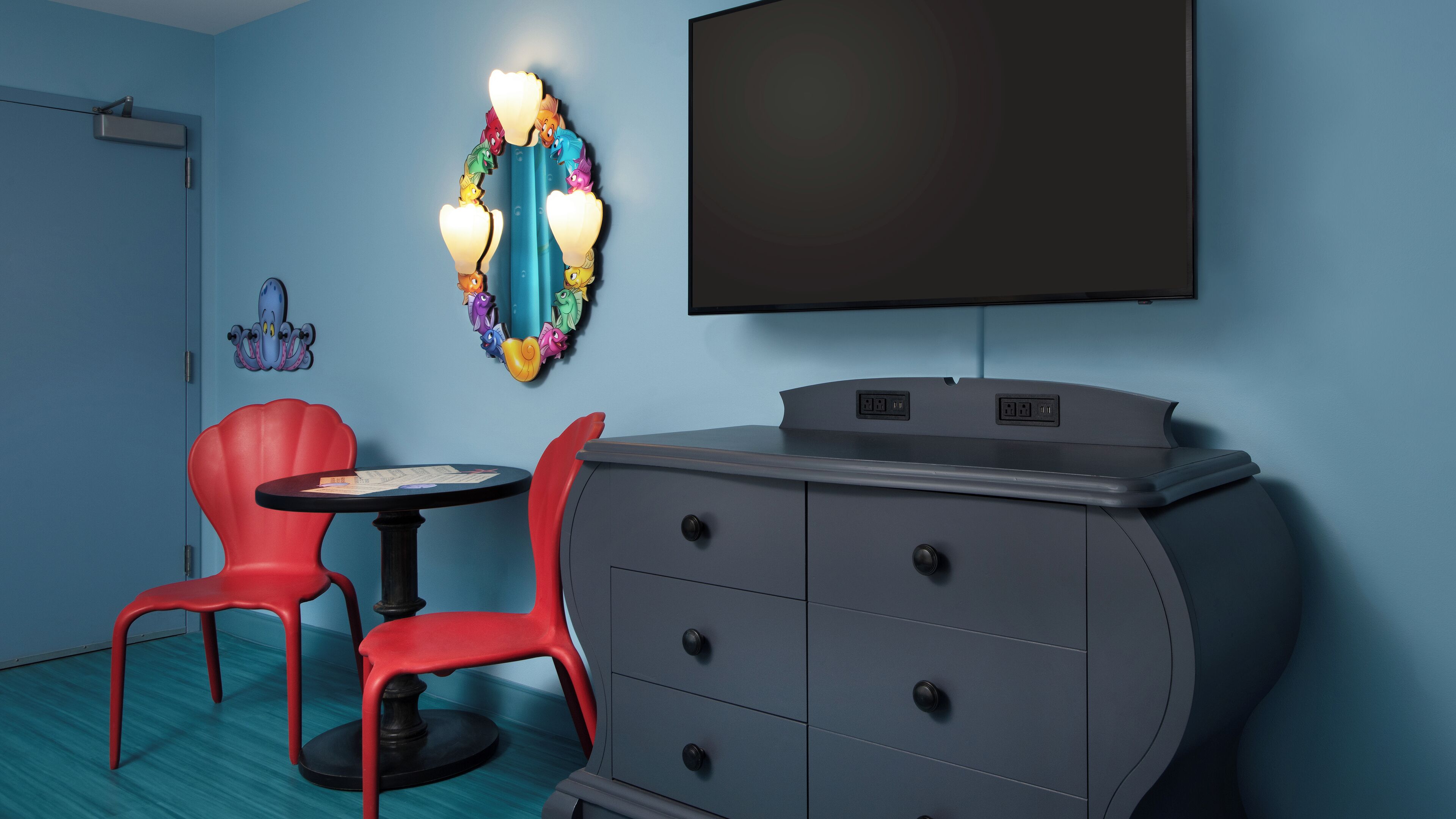 A room with a TV, a dresser, and two red chairs.